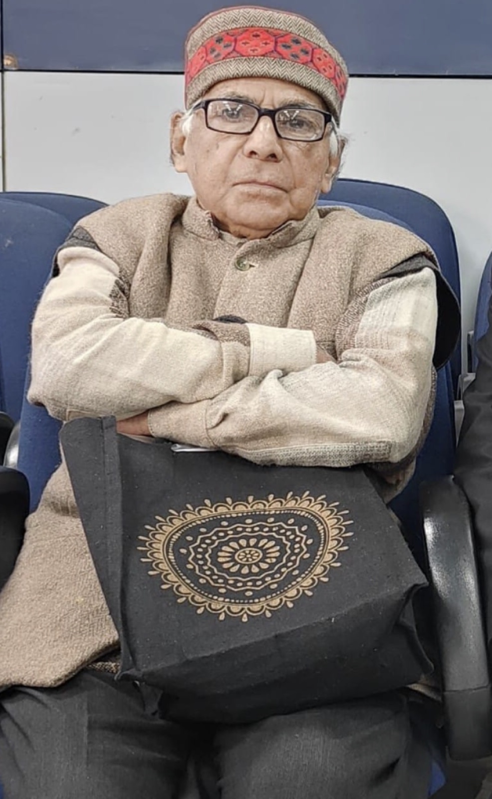 A dignified portrait of Prof. Ashok Kumar Gupta in a Himachali topi and vest, arms folded, seated at an event.