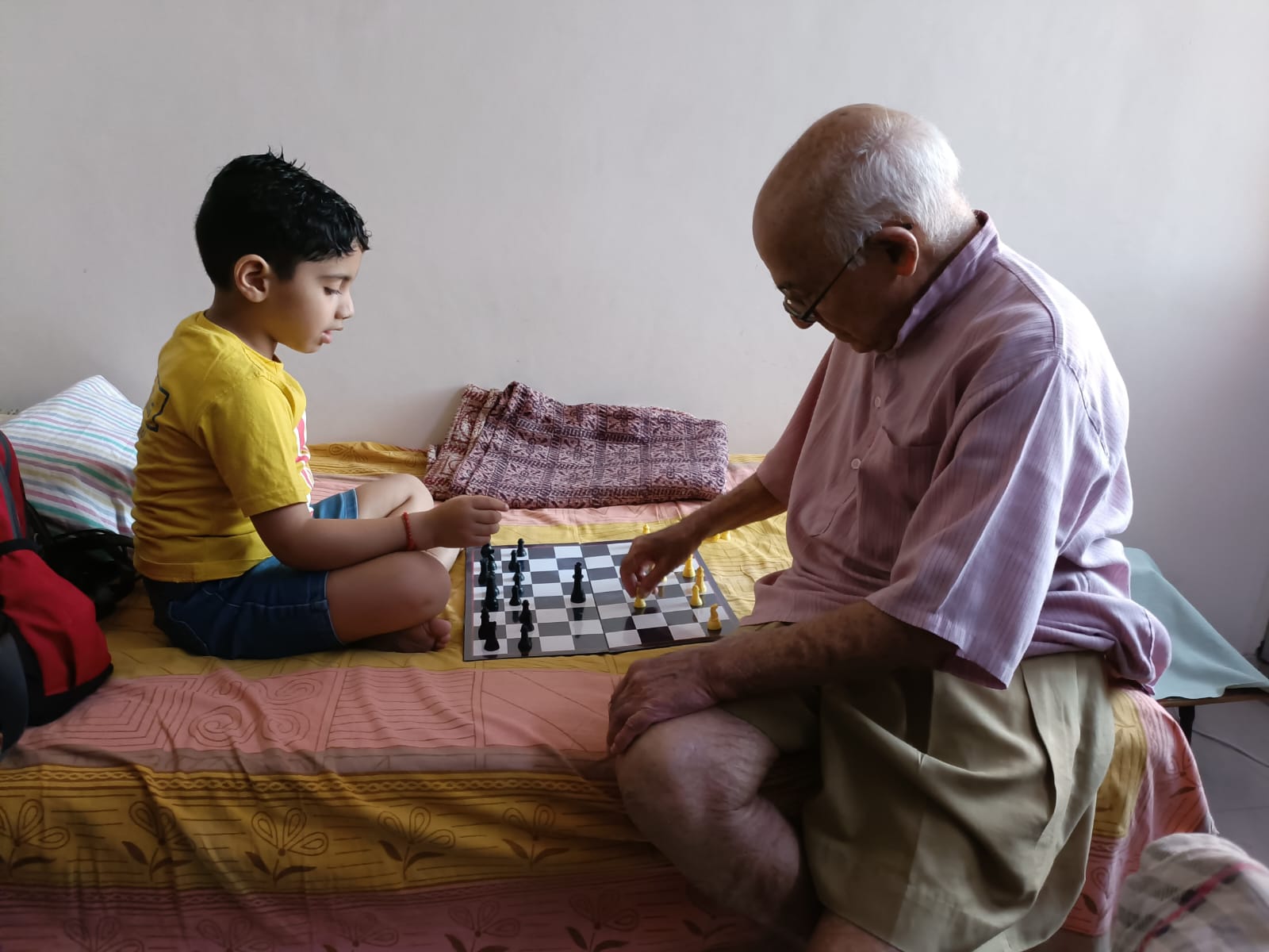 Prof. Gupta playing chess on a bed at home with a young boy.